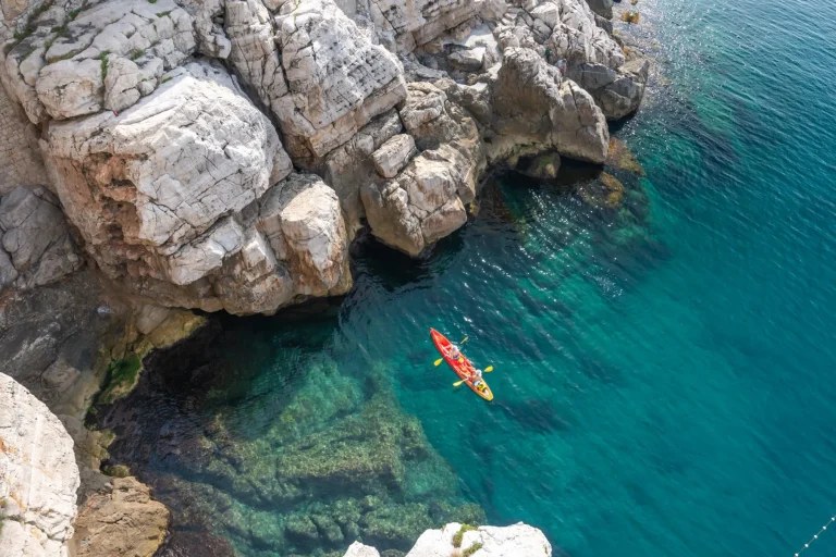 Vista dalle scogliere di roccia di un kayaker che esplora le acque cristalline del Mediterraneo in un'insenatura al largo della costa di Dubrovnik, Croazia